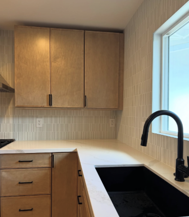 Kitchen with wooden cabinets, white countertop, black sink, and a window