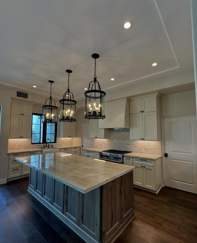 Modern kitchen with white cabinets, a marble kitchen island, black pendant lights, and hardwood floors.