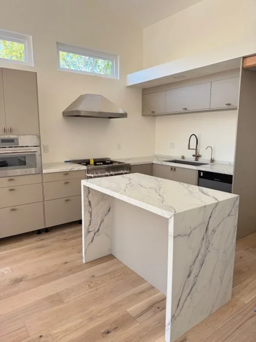 Modern kitchen with marble island, beige cabinetry, stainless steel appliances, and a minimalist design.