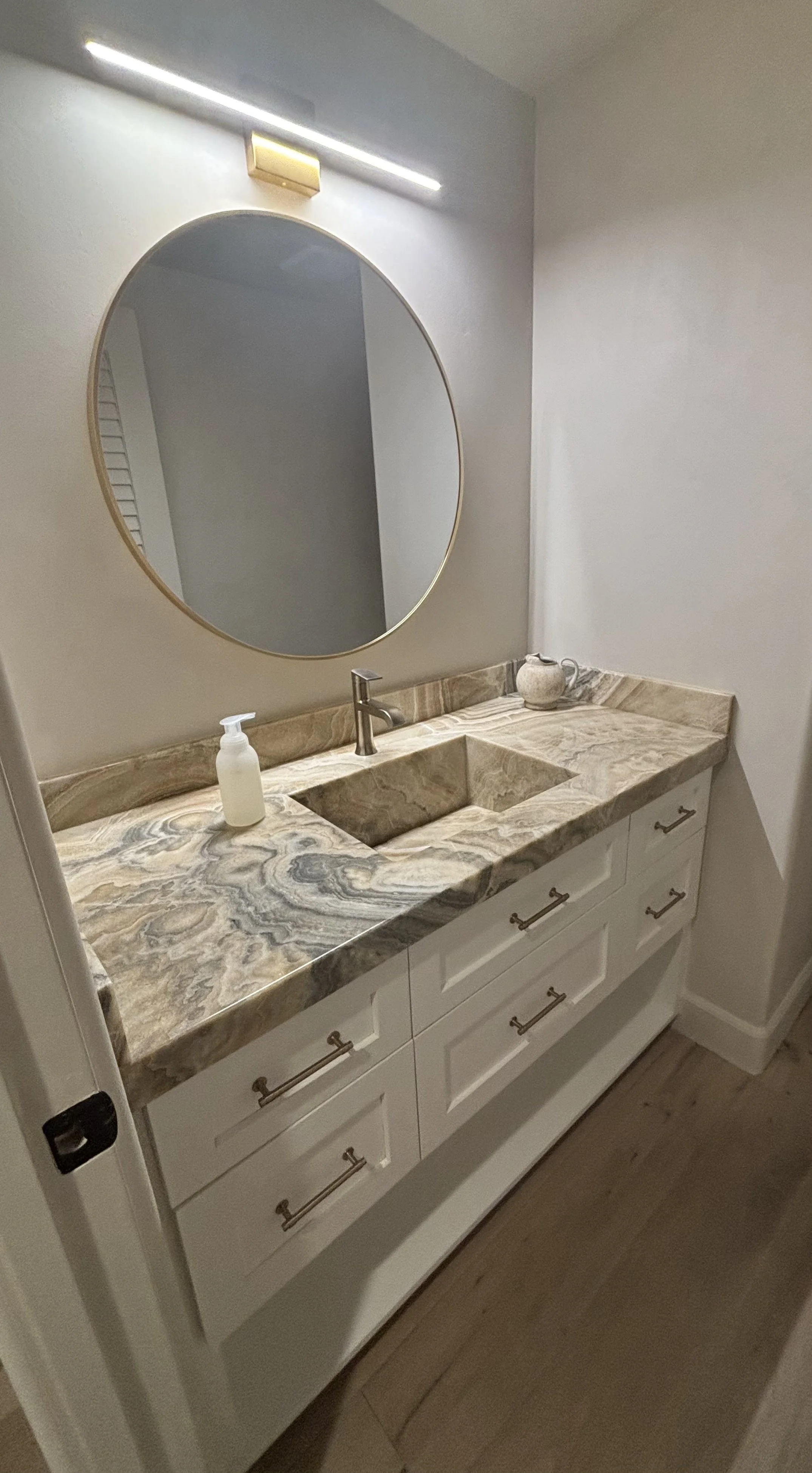 Bathroom vanity with a marble countertop, oval mirror, and soap dispenser.