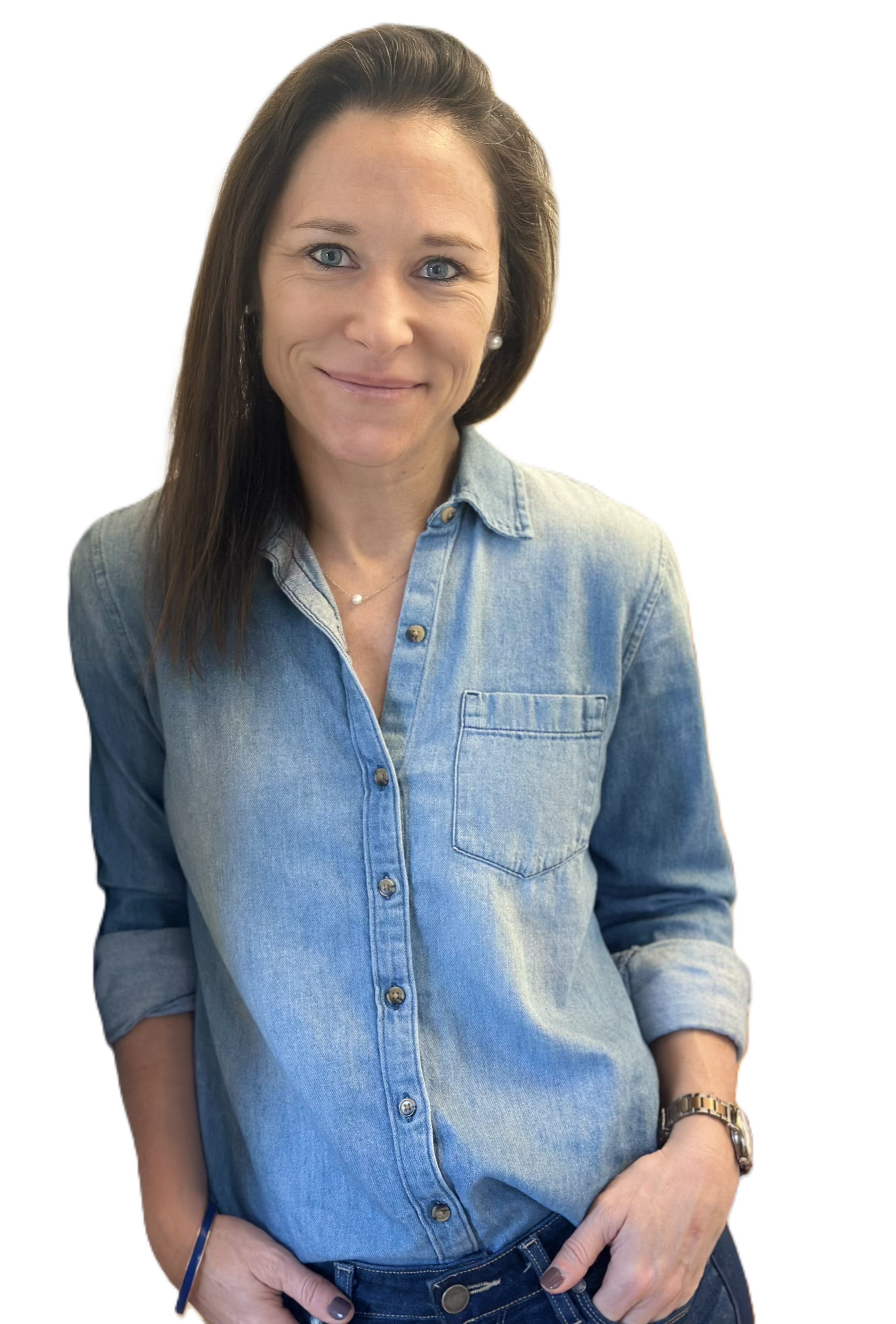 A woman with long brown hair, blue eyes, and a friendly smile, wearing a light blue denim shirt with rolled-up sleeves, a wristwatch, a delicate necklace, and pearl earrings.