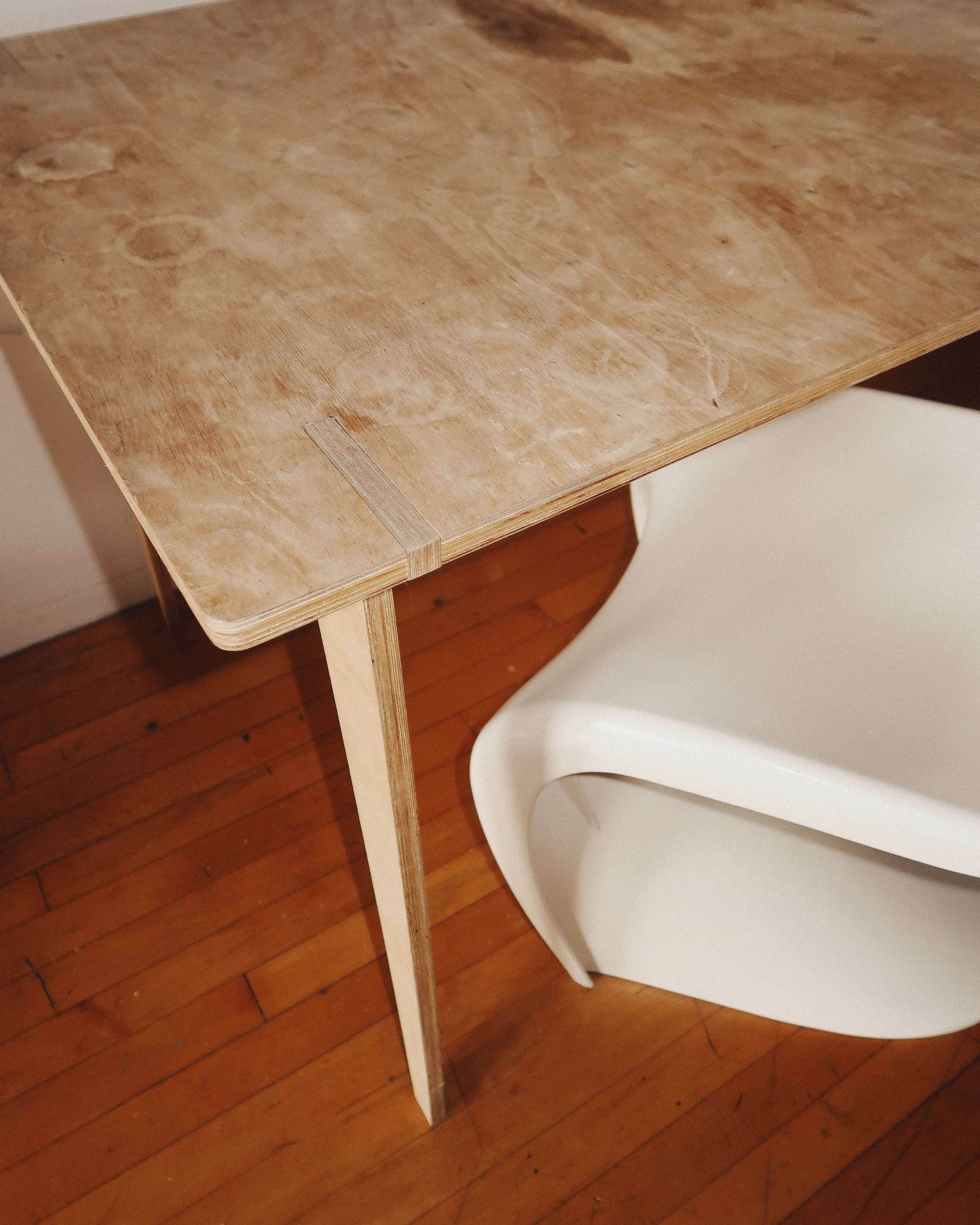 Mid-century modern plywood dining table with bent-leg construction, silver brackets for stability, and a lived-in patina.