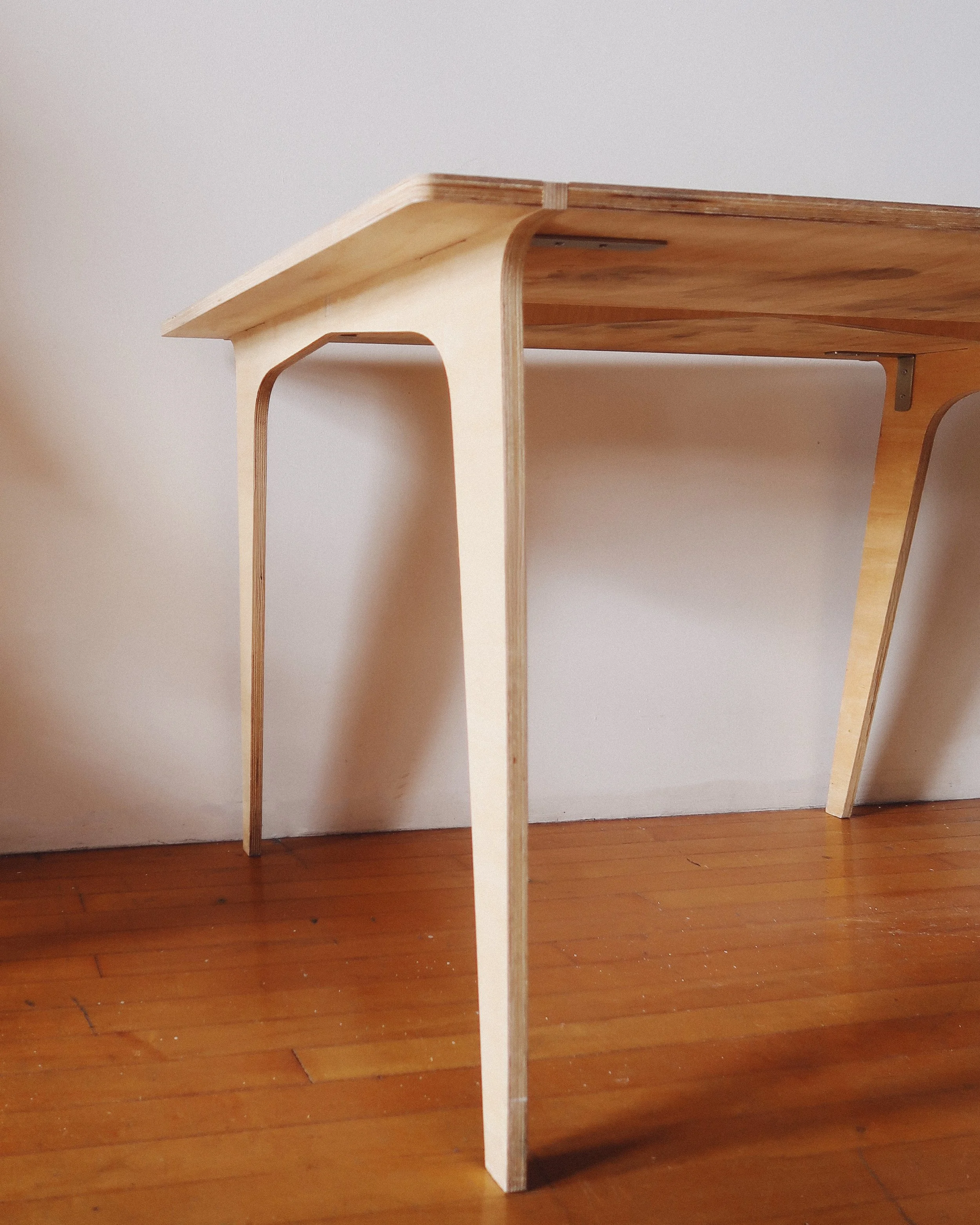 Mid-century modern plywood dining table with bent-leg construction, silver brackets for stability, and a lived-in patina.