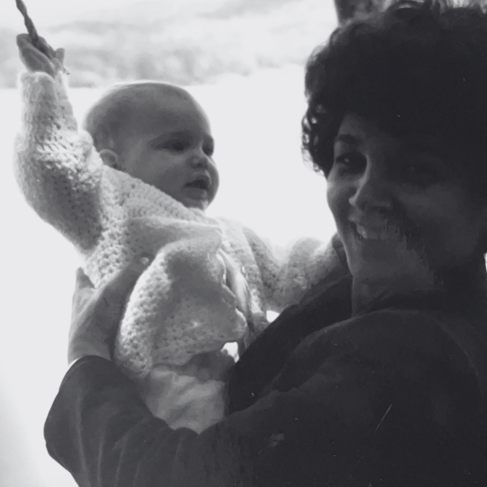 Carmela holding a baby and smiling at each other, both dressed warmly, in a black and white photo.
