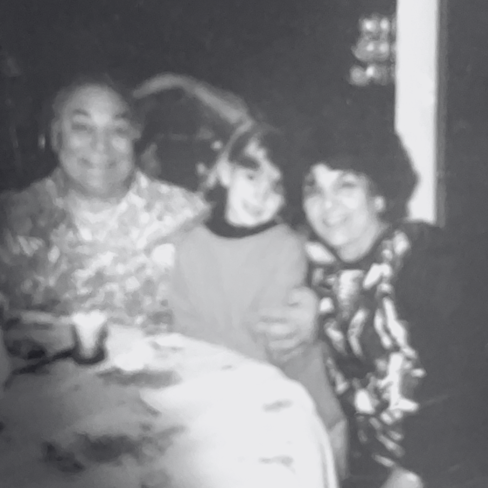 Three women sitting together at a table, smiling in a black and white photo.