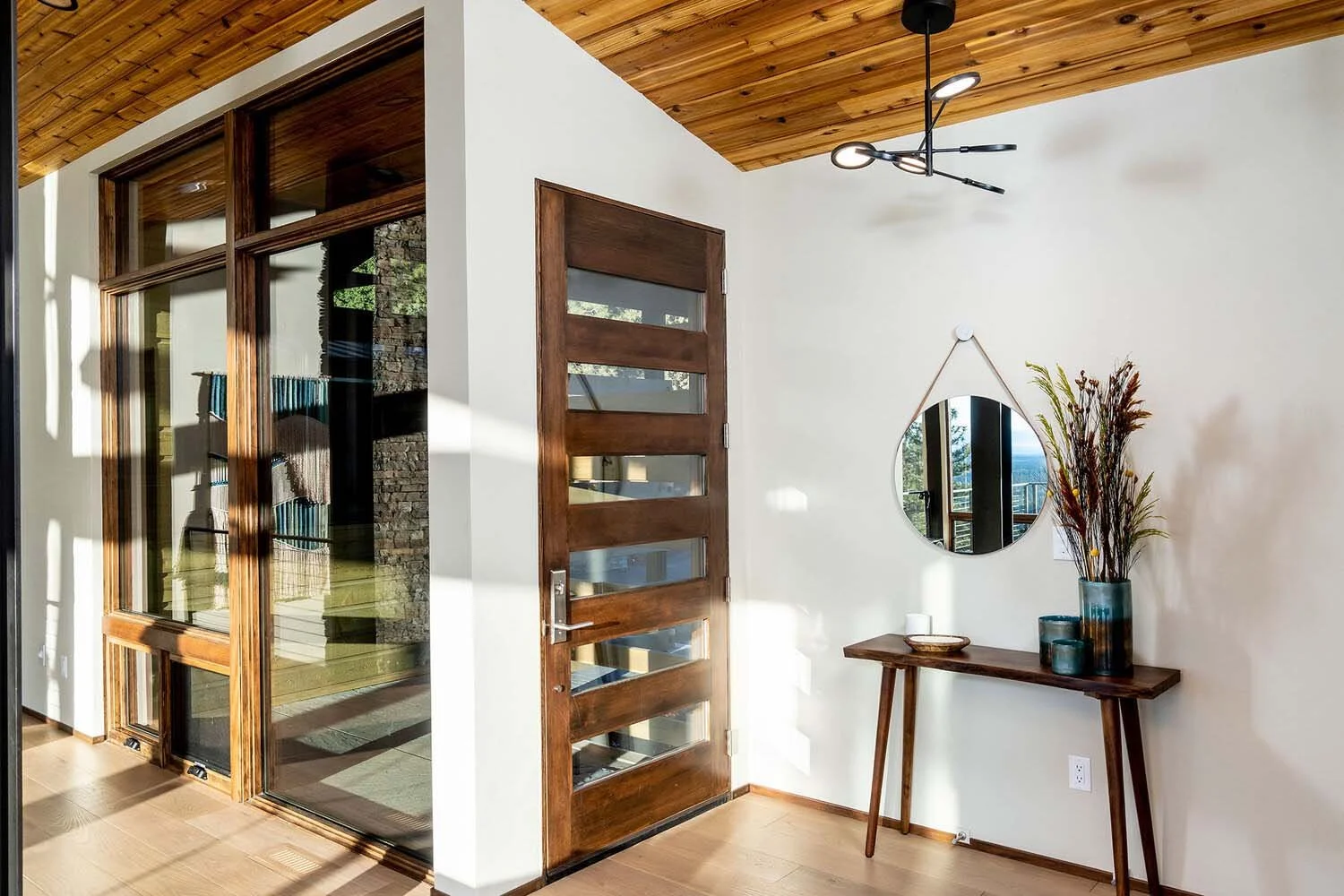 Highlighting the stunning architectural details of a Pacwest Builders' custom home, this image shows a unique interior nook. A dramatic wooden ceiling is complemented by a bold wooden door with horizontal glass panels, adding a touch of modern design