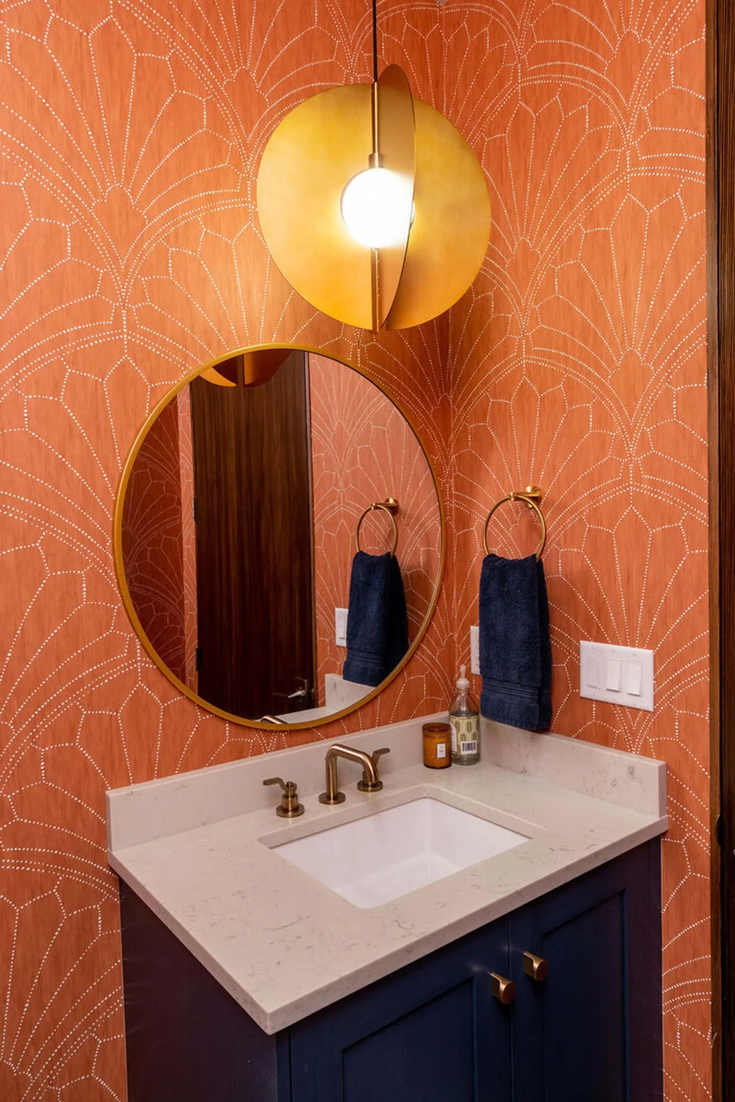 This modern bathroom, a showcase of Pacwest Builders' expert construction and interior design, highlights a stunning vanity area. The deep navy blue cabinet and luxurious marble countertop are complemented by a chic round mirror and elegant brass fix