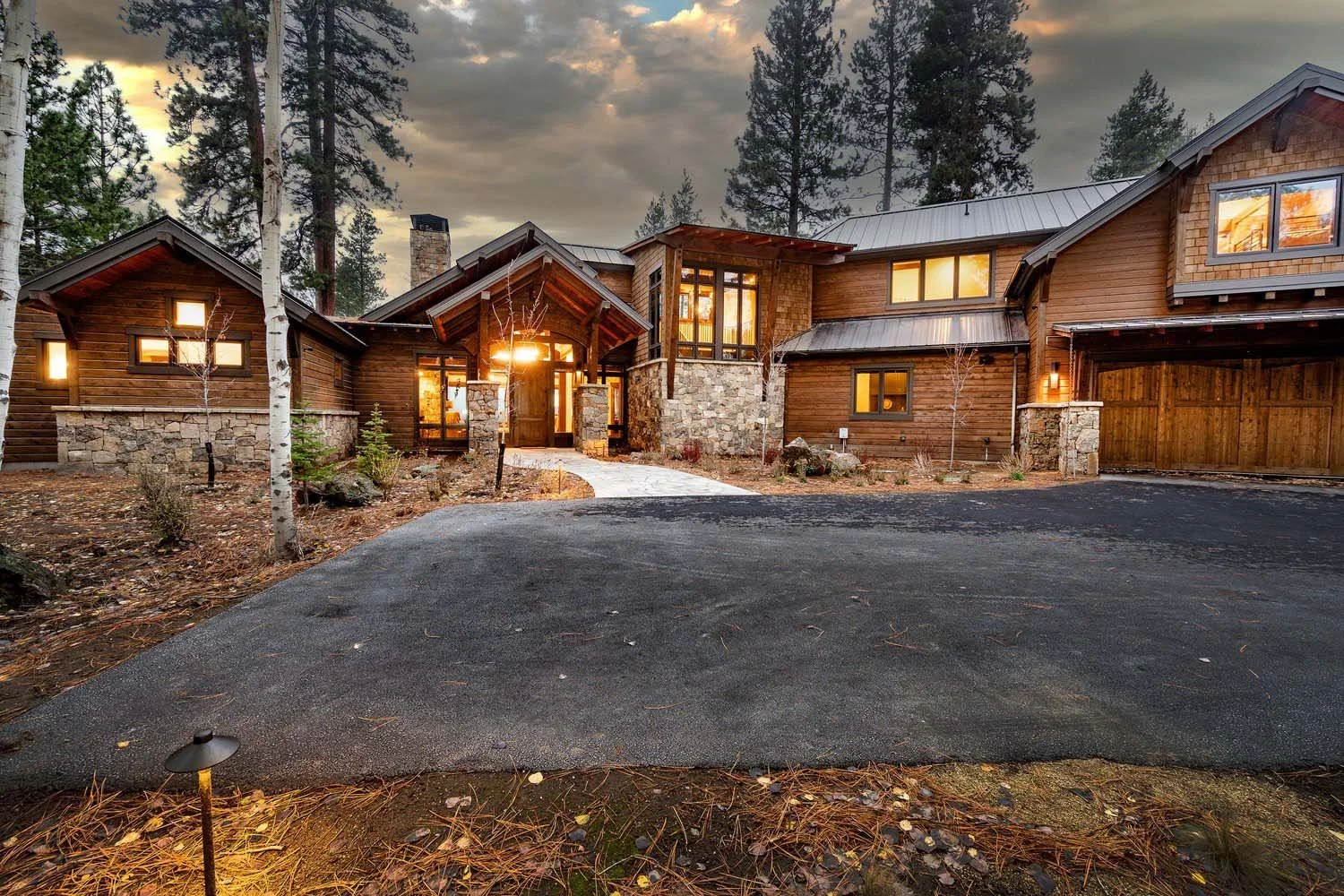 This expansive view of the Black Butte Ranch - Bishops Cap home by Pacwest Builders showcases its impressive mountain modern design and thoughtful integration. The large modern house features a striking wooden exterior with elegant stone accents, ref