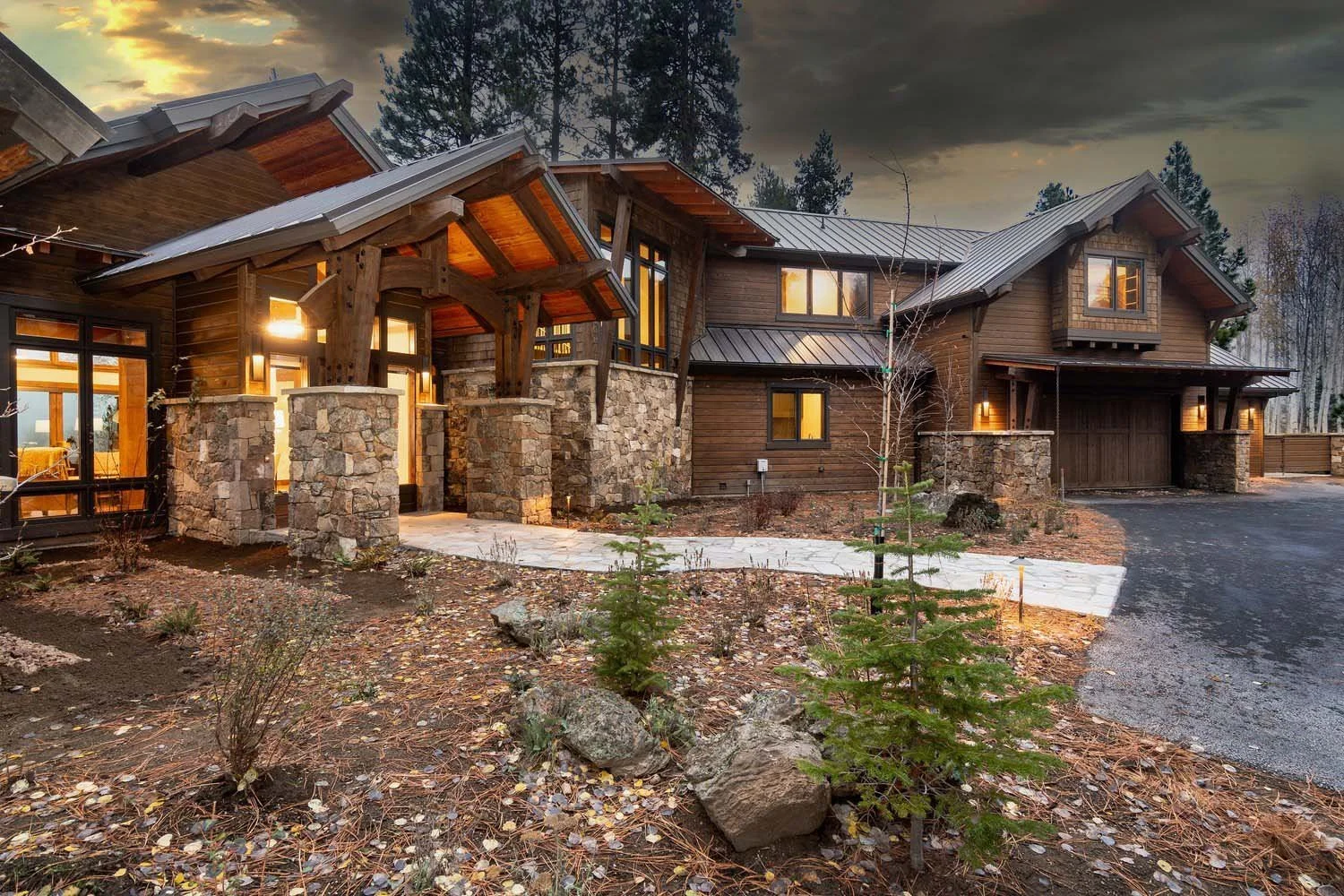 This breathtaking view of the Black Butte Ranch - Bishops Cap home by Pacwest Builders perfectly illustrates its seamless integration into the Central Oregon landscape. The large modern house, with its striking wood and stone exterior, glows warmly f