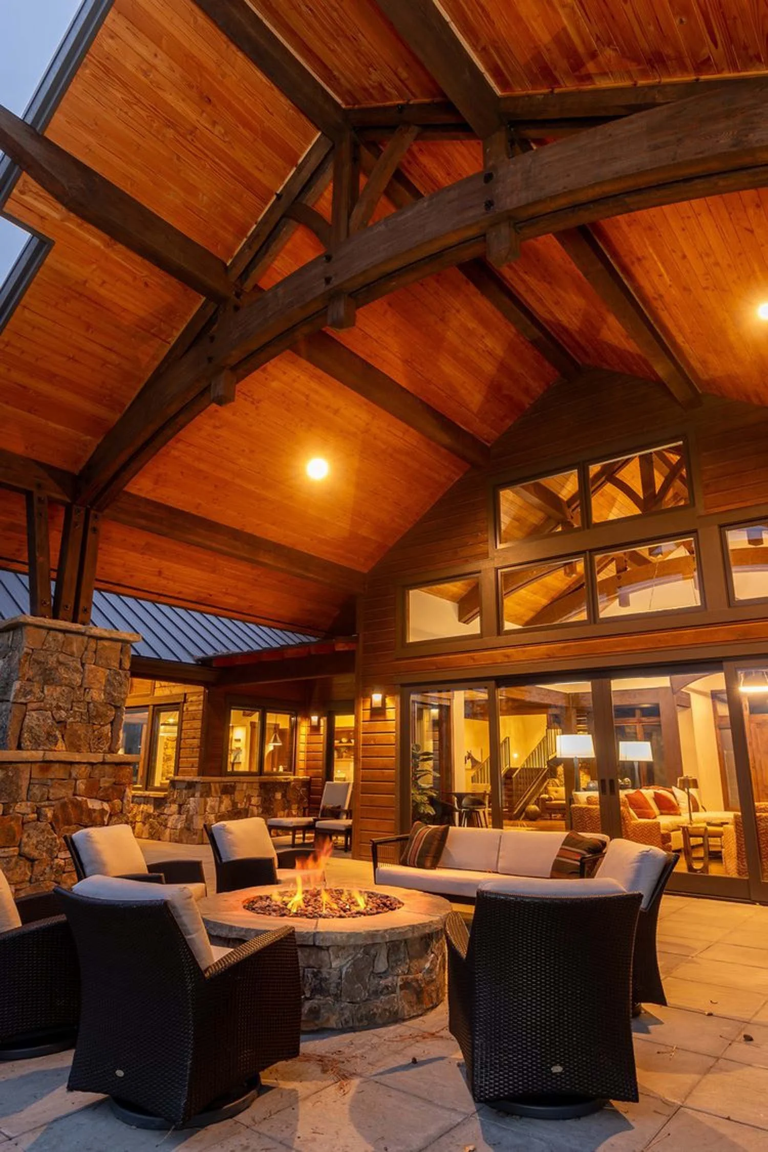 This luxurious outdoor patio at Black Butte Ranch - Bishops Cap is an ideal gathering spot, expertly designed by Pacwest Builders. A central fire pit, surrounded by comfortable chairs, creates a warm and inviting atmosphere, all sheltered under a mag