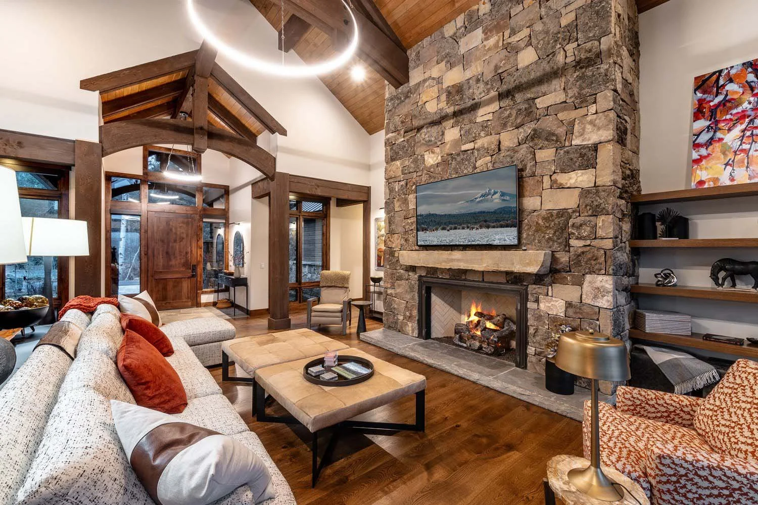 This stunning living room at Black Butte Ranch - Bishops Cap, a perfect retreat getaway, is a showcase of the masterful architectural design by Steve Van Sant. The centerpiece is a magnificent large stone fireplace with a mounted TV, creating a cozy