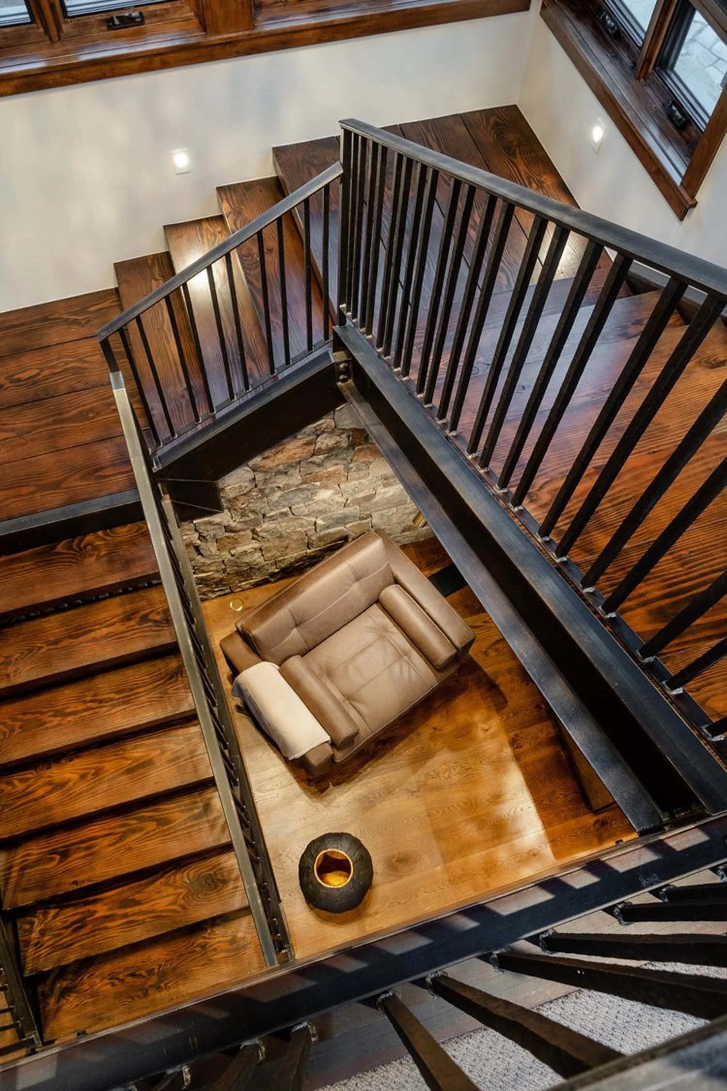 A dramatic, high-angle view showcases the elegant transition from the upper level to a cozy living space, a hallmark of Pacwest Builders' experienced architects' design. The bespoke wooden staircase with sleek black railings serves as a central featu