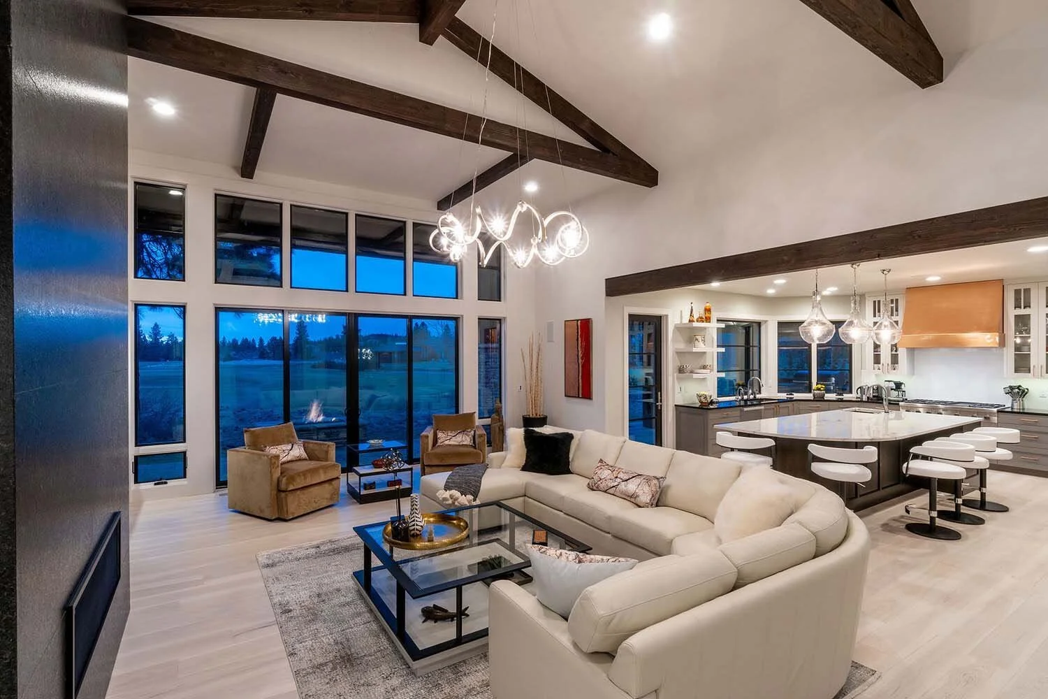 Experience the grandeur of this modern open-concept living room and kitchen, a signature of Pacwest Builders' luxury custom homes. Soaring high ceilings and magnificent wooden beams create an expansive and inviting atmosphere. Large windows flood the