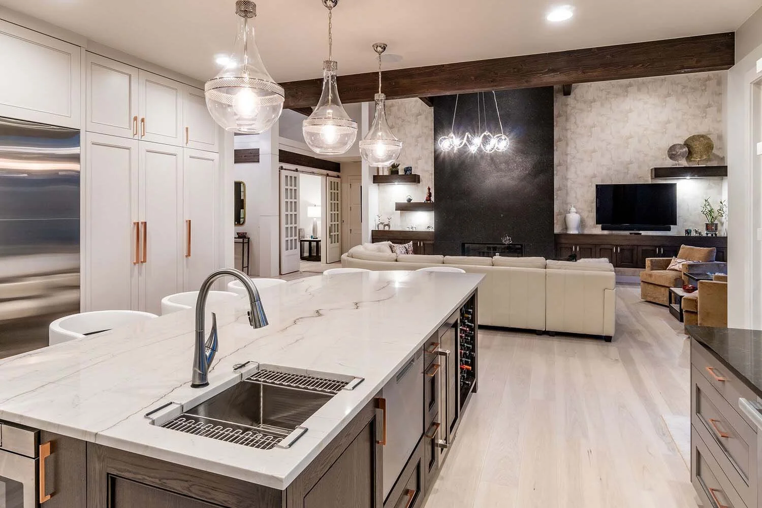 This exquisite modern open-concept kitchen, designed by Pacwest Builders, features a grand marble island that seamlessly flows into the inviting living room. Sleek white cabinetry, elegant pendant lights, and a sophisticated fireplace create a luxuri