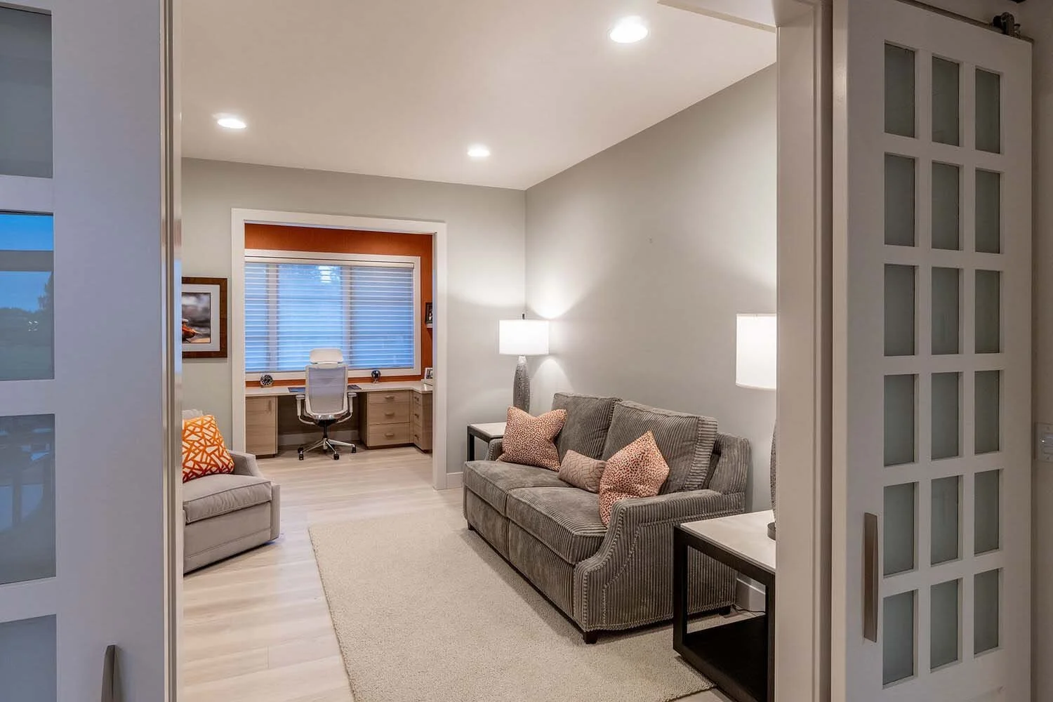 This refined office space, a showcase in a luxury custom home by Pacwest Builders, offers a seamless transition from a comfortable lounge area to a productive workspace. The seating area features a sophisticated gray sofa, armchair, and side table wi