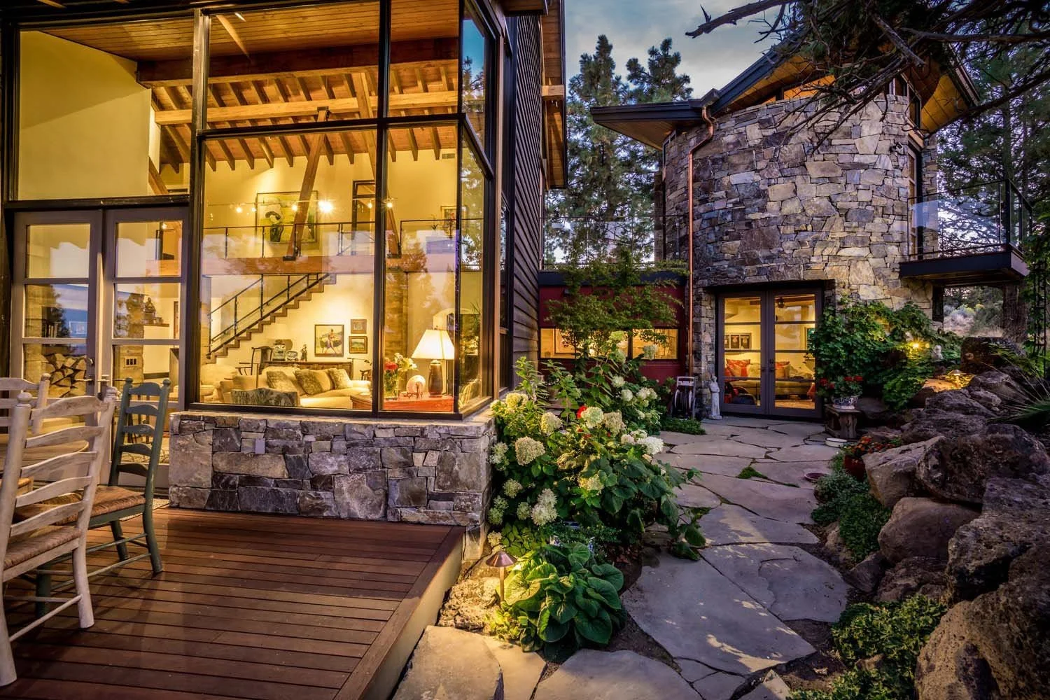 Capturing the essence of North Rim, this modern home, a luxury custom home collaboration between Hayes Inc. design and Pacwest Builders' expertise, boasts striking stone walls and expansive glass windows. Illuminated in the evening, this Central Oreg