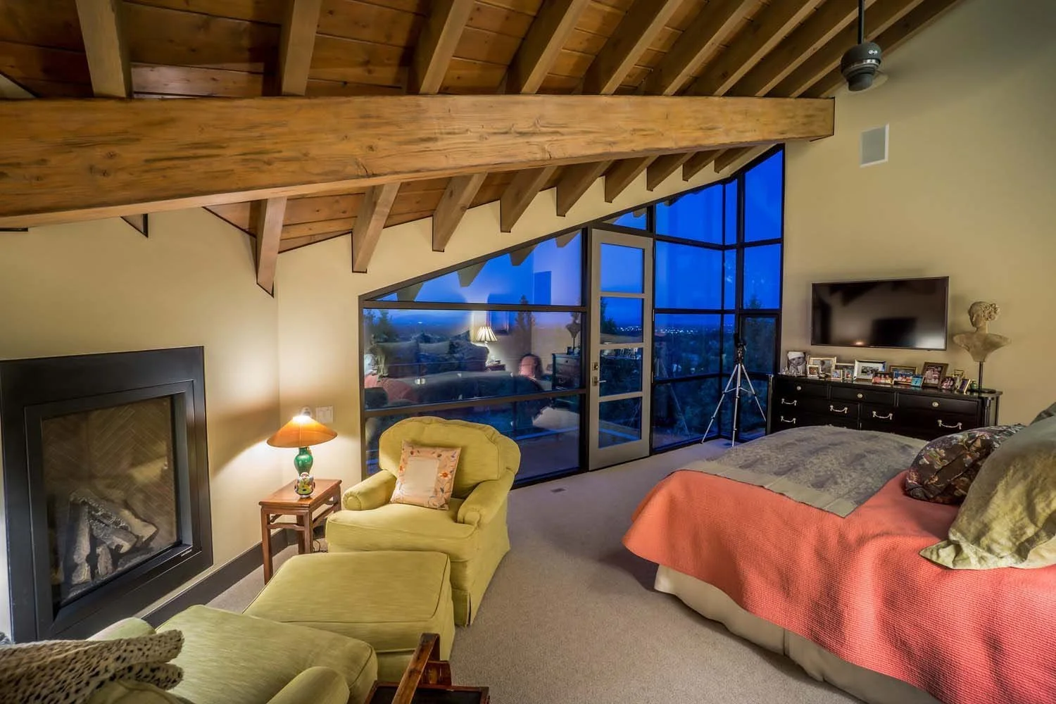 This incredibly cozy bedroom, a tranquil sanctuary in a luxury custom home built by Pacwest Builders with Hayes Inc. design in North Rim, showcases a distinctive sloped wooden ceiling. A large window frames a captivating view of the outside landscape