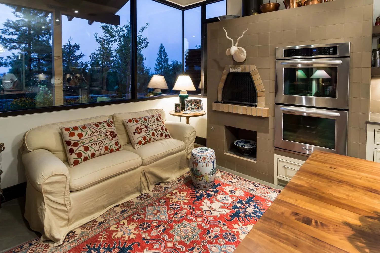 This exceptionally cozy living room, a key space within a luxury custom home built by Pacwest Builders with Hayes Inc. design in North Rim. A small side table with lamps, a decorative ceramic stool, and a vibrant colorful area rug enhance the invitin