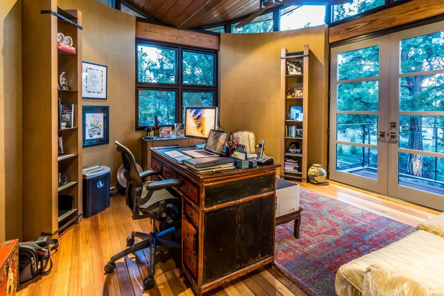 This sophisticated home office, a functional and inviting space in a luxury custom home built by Pacwest Builders with Hayes Inc. design in North Rim, features rich wooden floors. Large windows frame picturesque views of the outside trees, while the