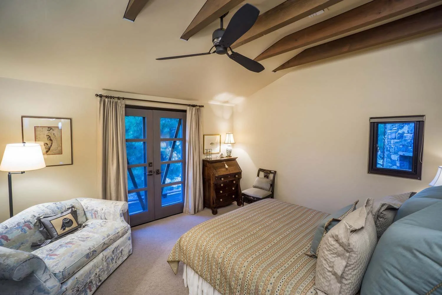 This charming and cozy bedroom, a unique space within a luxury custom home built by Pacwest Builders with Hayes Inc. design in North Rim, offers a delightful retreat. A comfortable bed and a floral sofa with a decorative pillow create an inviting sea