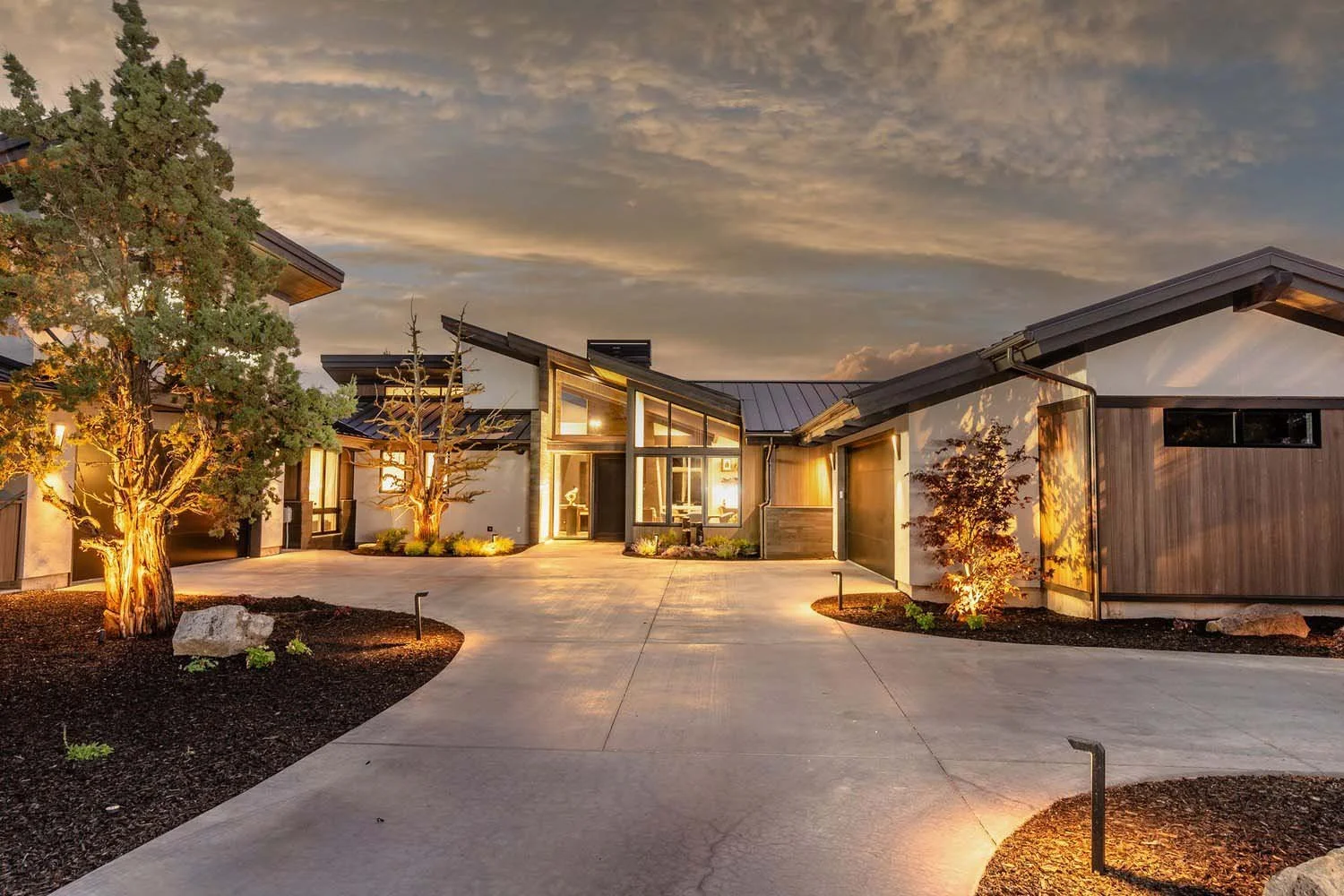 This wider view of the Pronghorn - Canyon View home showcases its strategic design by Blair Davis. The mountain modern residence features a unique wood-paneled garage door and a meticulously landscaped front yard that complements the home's striking
