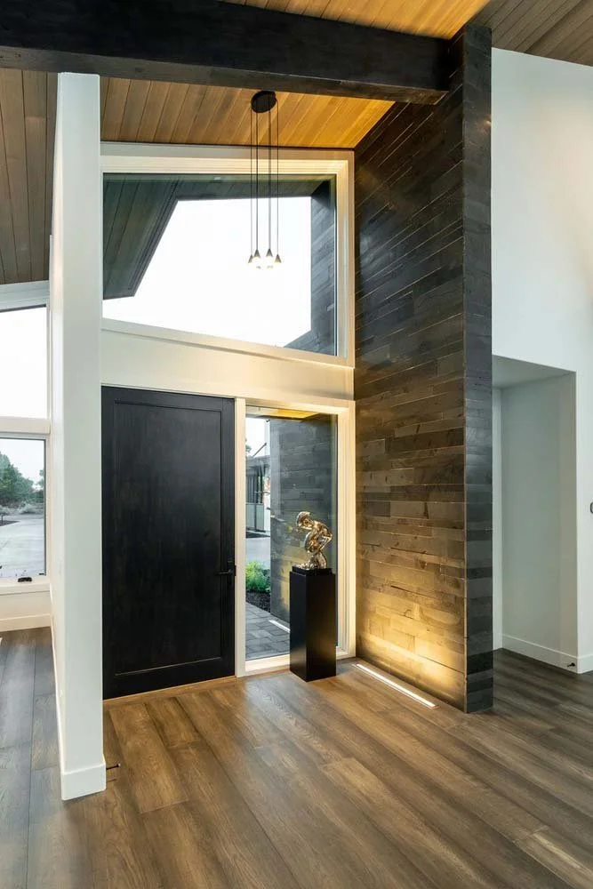 The impressive entryway of the Pronghorn - Canyon View home, designed by Blair Davis, beautifully combines natural materials with unique architectural features. A custom dark wood door and a prominent stone siding wall create a striking contrast, whi