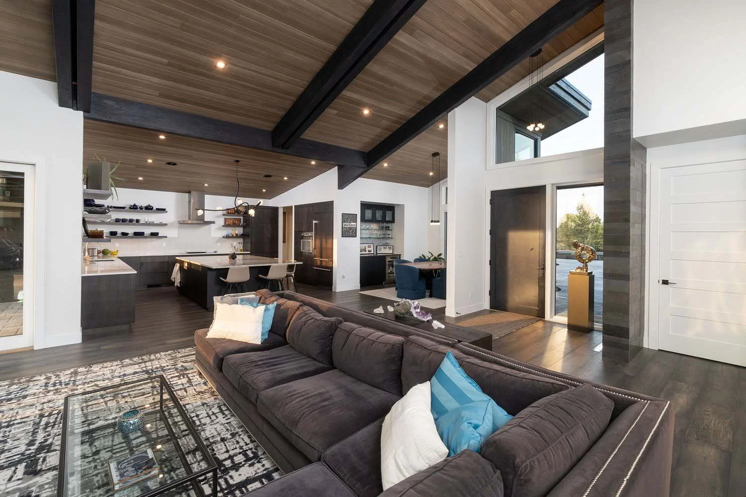 This breathtaking open-concept living room and kitchen at Pronghorn - Canyon View is a masterpiece of mountain modern design by Blair Davis. The space is flooded with natural light from its high vaulted ceiling and expansive large windows. The living