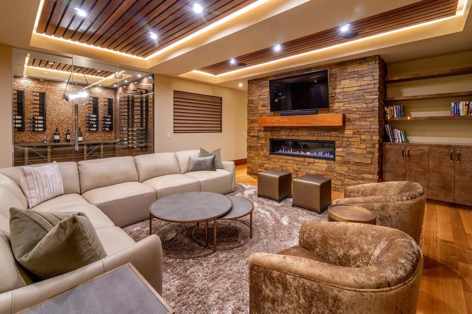 As experienced builders of luxury custom homes in Central Oregon, Pacwest Builders crafted this unique living space at North Rim - Wild Rye. The design features illuminated wood-paneled ceilings near an open bar. A cozy beige sectional sofa and a bea