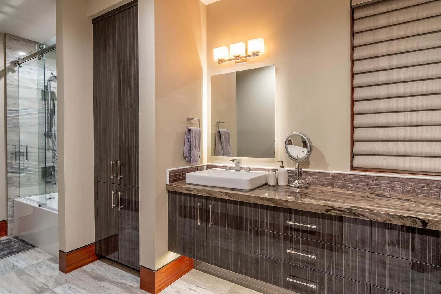 This stunning bathroom in the North Rim - Wild Rye home by Pacwest Builders is a testament to sophisticated design. The space features a modern vanity with a sleek sink, a large mirror, and a beautiful light fixture. A spacious shower area provides a
