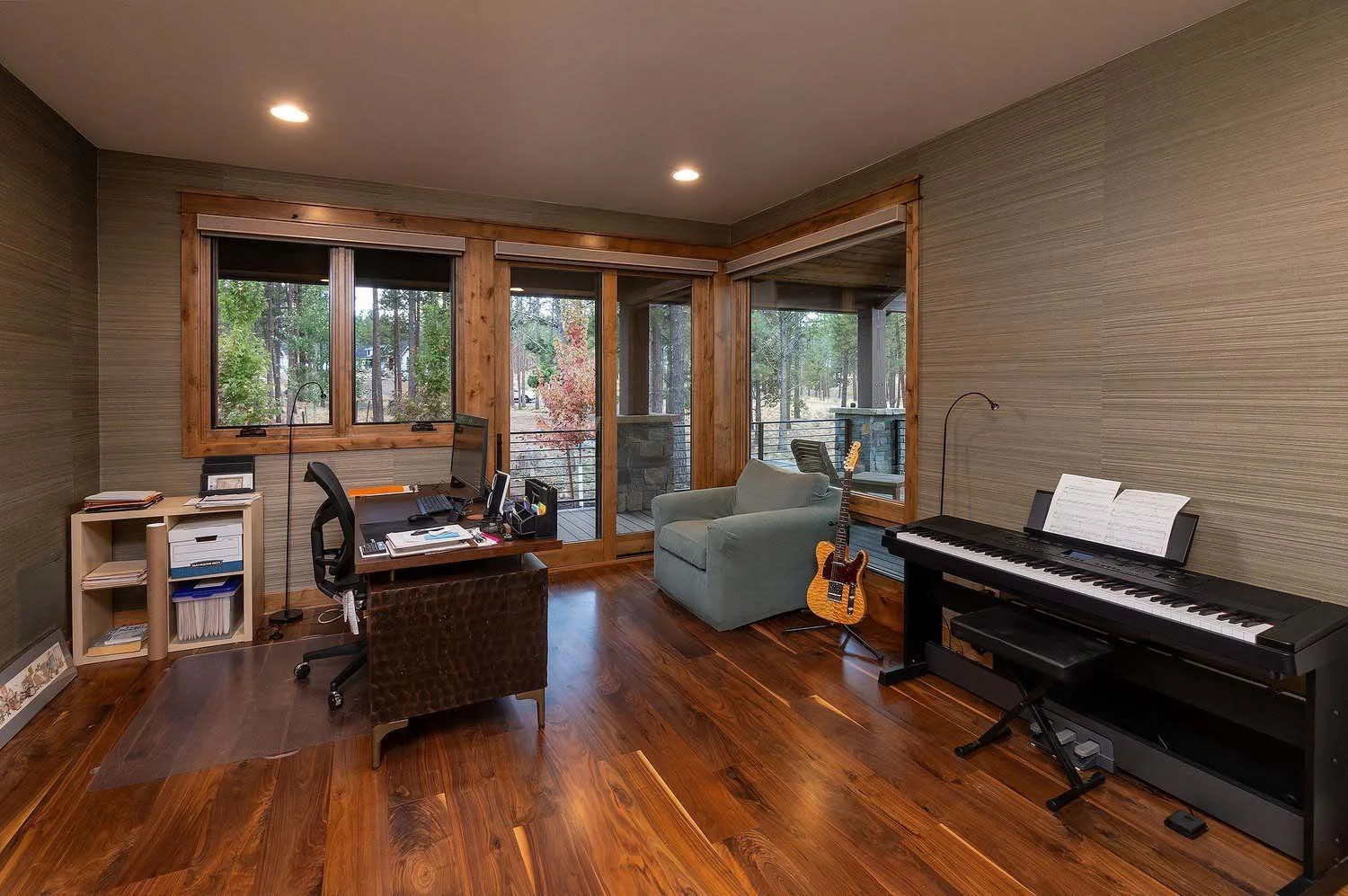 This sophisticated home office at the Skyline Ranch - Imbler home by Pacwest Builders is designed for both productivity and personal passion. Large windows provide a refreshing view of a wooded outdoor area, offering a peaceful escape.