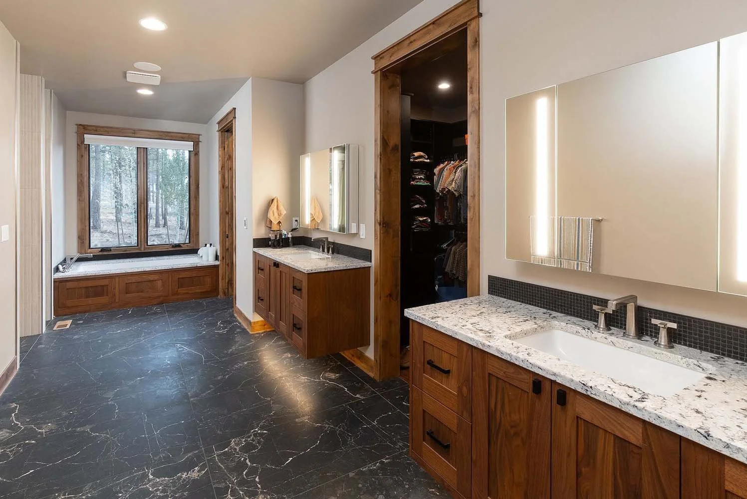 This stunning large bathroom at the Skyline Ranch - Imbler home by Pacwest Builders is a perfect blend of style and functionality. The space features two elegant wooden vanities with granite countertops and two large mirrors. The luxurious bathtub, p