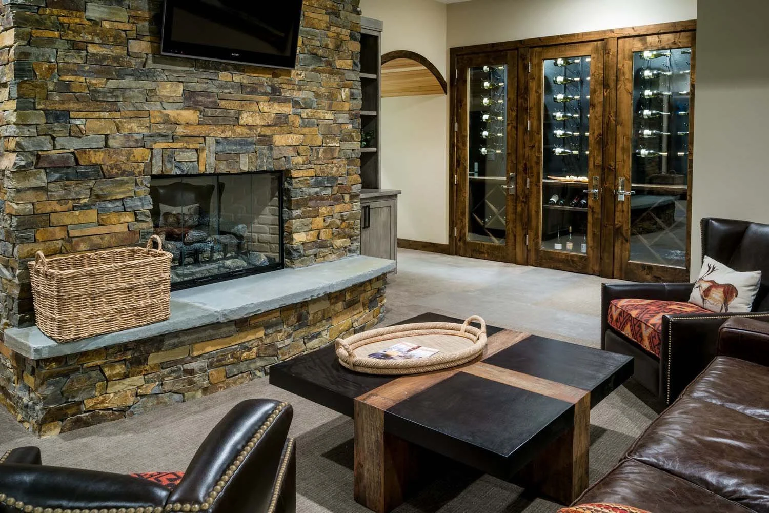 This inviting living room in the award-winning North Rim - Wild Rye home by Pacwest Builders is designed for comfortable gatherings. A magnificent stone fireplace creates a cozy focal point, while a custom wooden cabinet with wine bottles adds a uniq