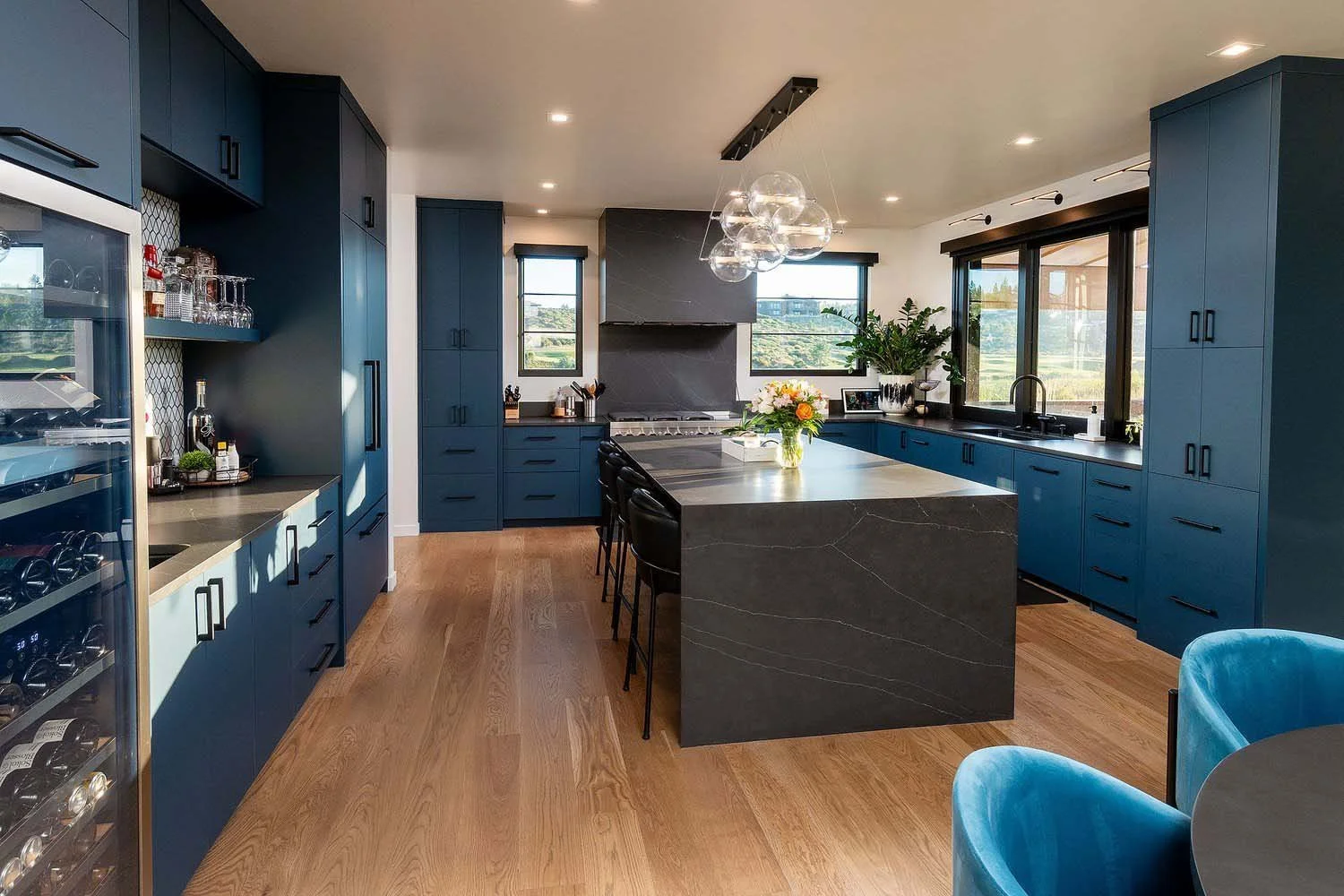 This spacious modern kitchen at Tetherow - Hardin Martin Court by Pacwest Builders is a perfect blend of style and functionality. The space features elegant blue cabinets, sleek black countertops, and a magnificent large island. Expansive large windo