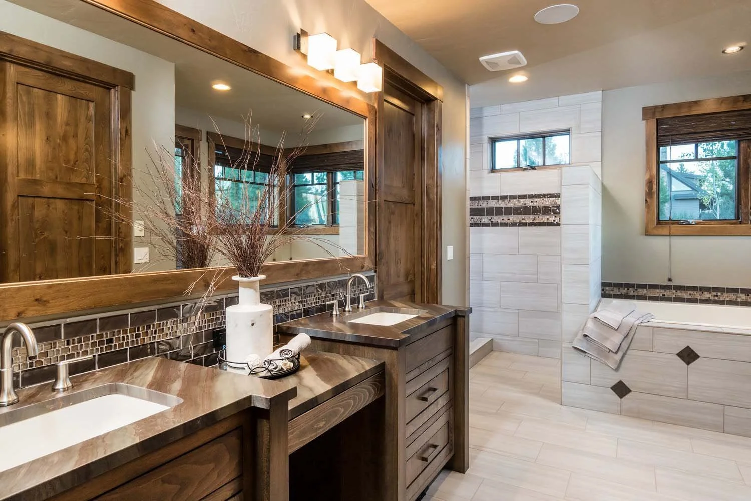 This elegant bathroom at Tetherow - Hawk Court by Pacwest Builders is a testament to sophisticated design and functionality. The space features a custom vanity with dual sinks and beautiful wooden cabinets, complemented by a large mirror. The spaciou