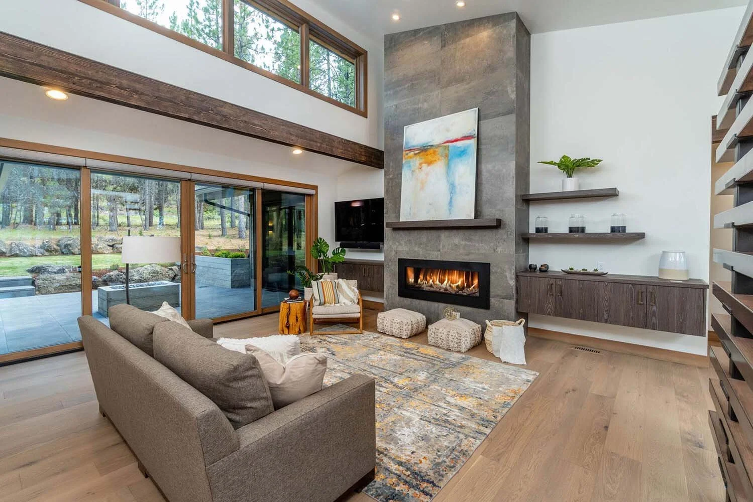 This stunning living room at Tetherow - Meeks Trail by Pacwest Builders is a perfect blend of modern design and nature. The space features expansive large glass sliding doors that overlook a beautiful garden with rocks and trees. The room is anchored