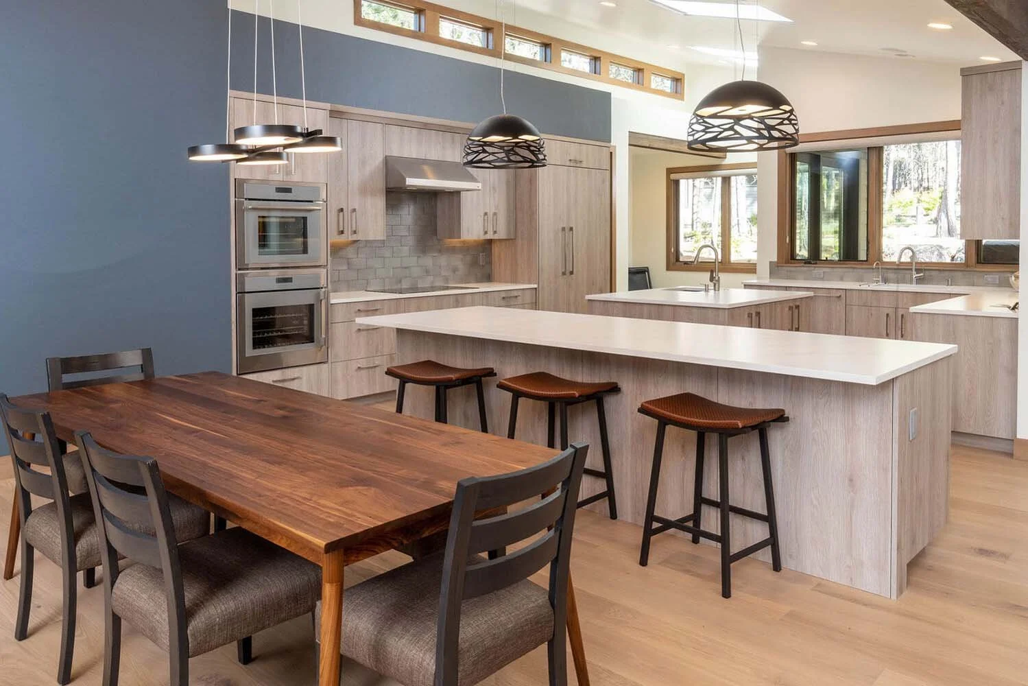 This stunning modern kitchen in the "Best of Show" winning home at Tetherow - Meeks Trail is a testament to sophisticated design and functionality. The space features elegant light wood cabinets and a beautiful large island with a white countertop an