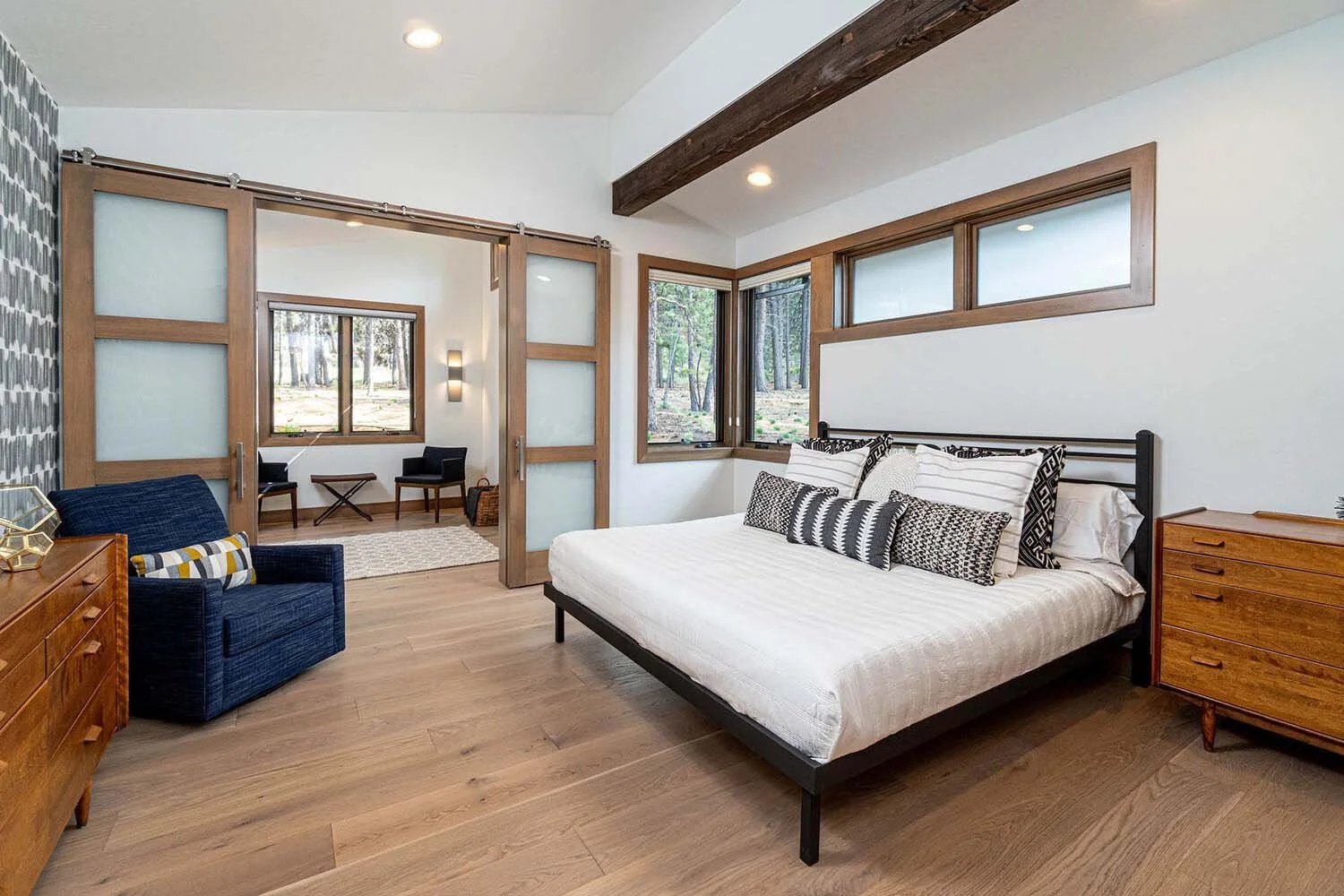 This peaceful bedroom in the "Best of Show" winning home at Tetherow - Meeks Trail by Pacwest Builders is a true retreat designed for comfort and style. The space features beautiful wooden flooring, a striking large bed with a black metal frame, and