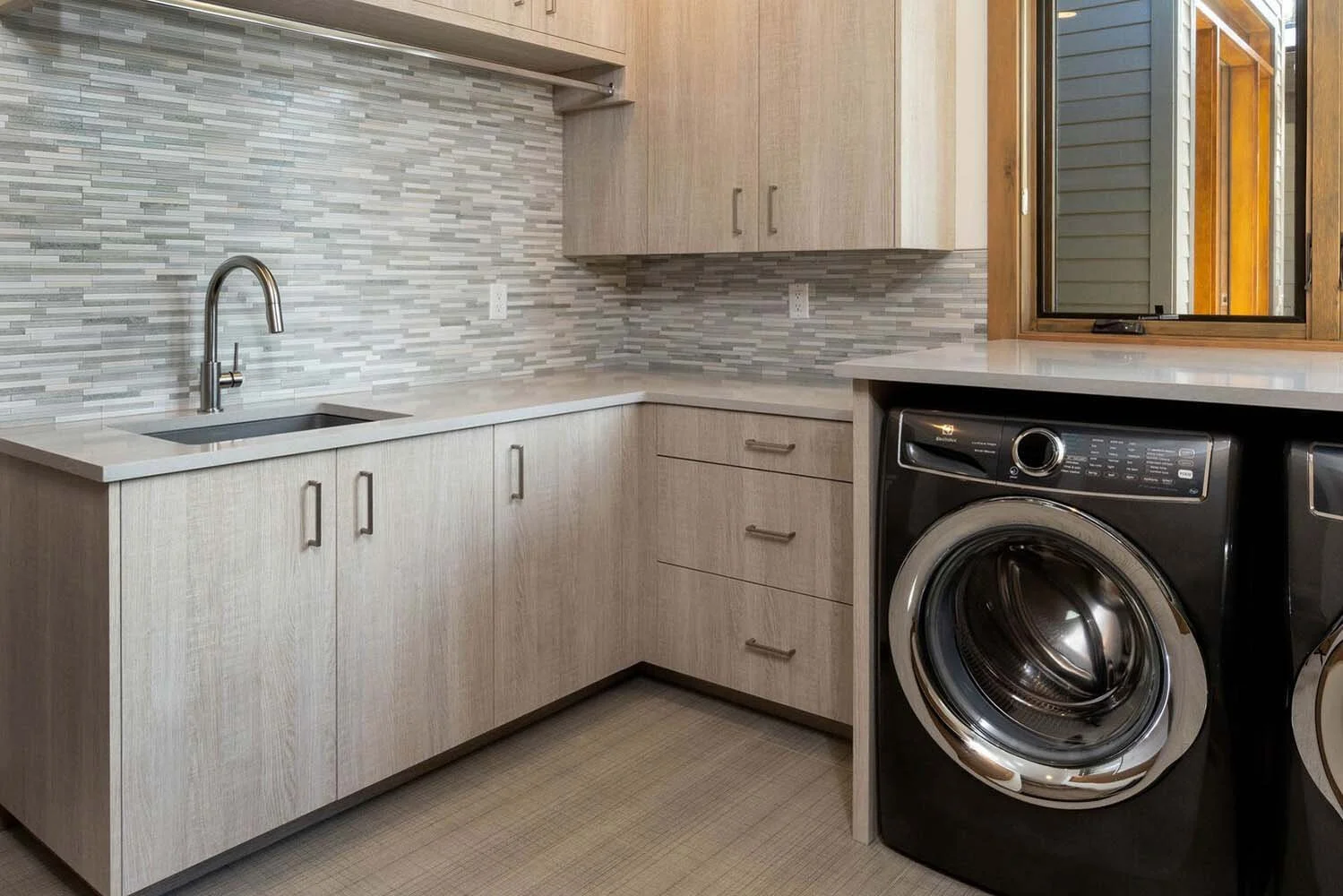This well-designed laundry room in the "Best of Show" winning home at Tetherow - Meeks Trail is a perfect blend of style and practicality. The space features a beautiful beige wooden cabinet that provides ample storage, and a washing machine perfectl