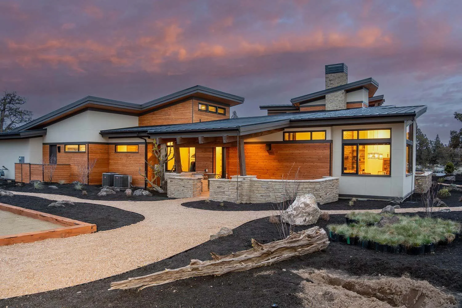 Luxury custom home in Pronghorn by Pacwest Builders. This Central Oregon residence, designed by Blair Davis, features a modern aesthetic with a mix of cedar, stone, and glass. The landscaped yard includes gravel pathways and rocks, leading to the hom