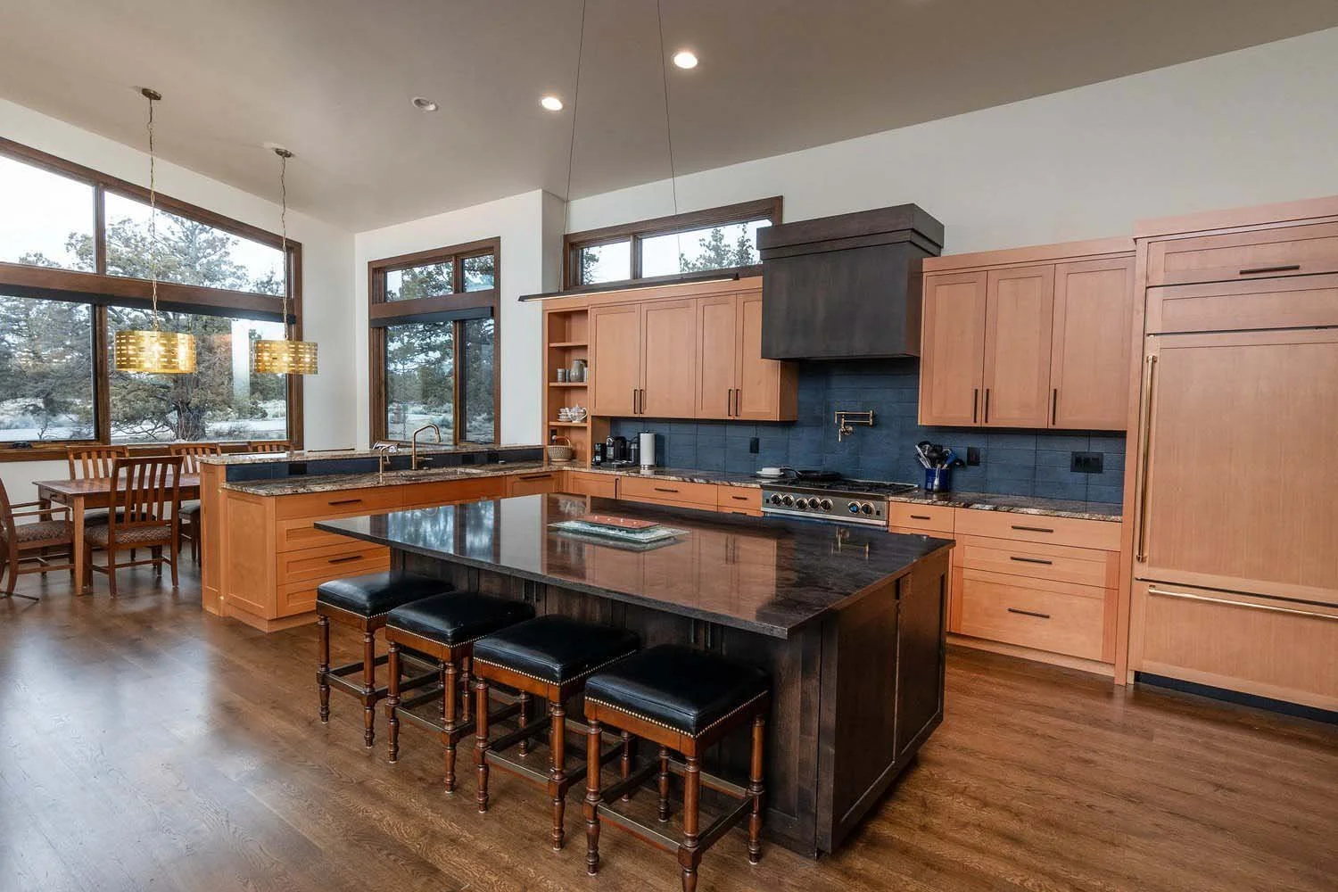 This modern kitchen in Pronghorn - Switchback, built by Pacwest Builders, is a perfect blend of style and function. The wooden cabinets and black countertops create a sophisticated look, while large windows with views of trees bring the beauty of Cen