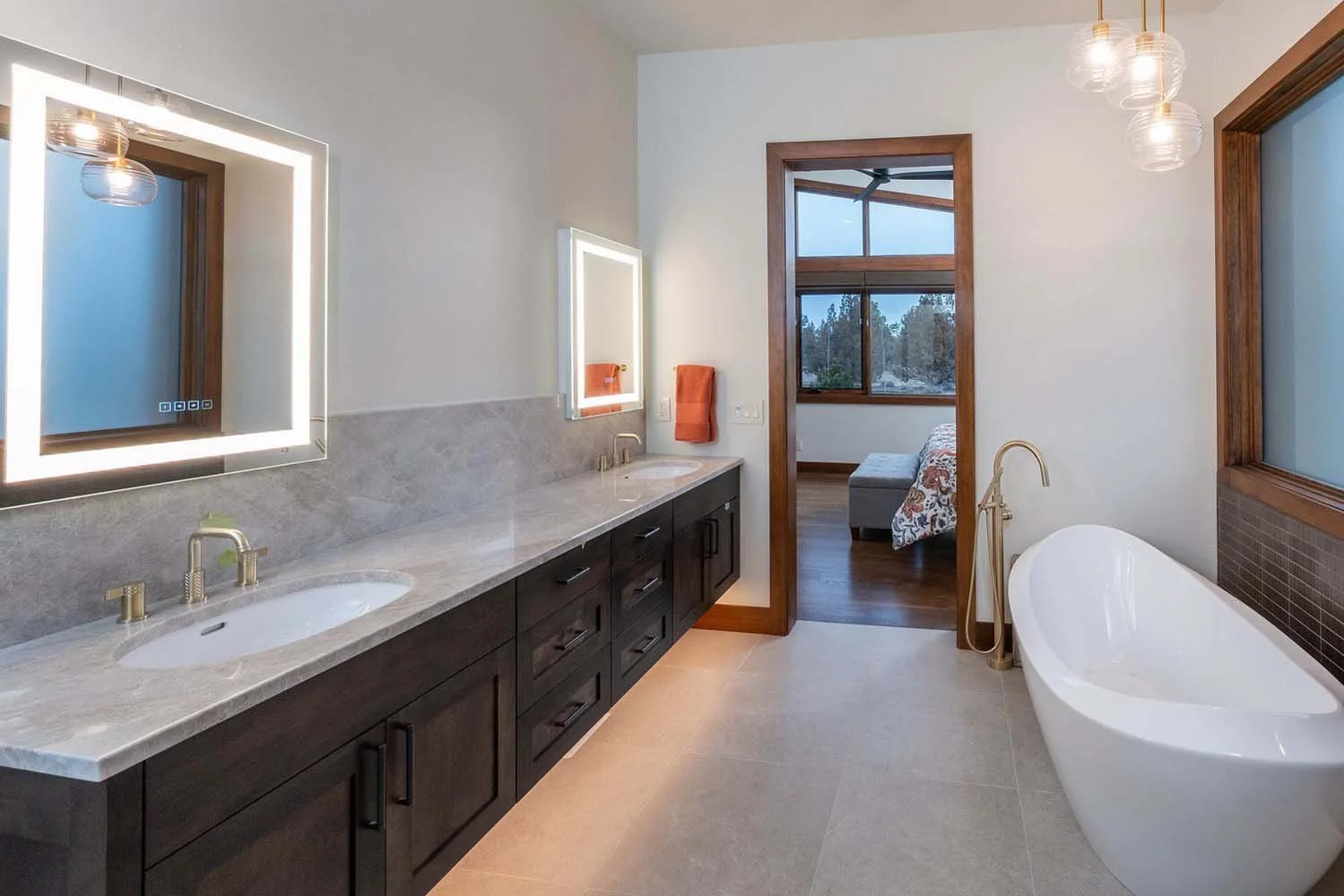This modern bathroom in Pronghorn - Switchback showcases the impeccable architecture of this luxury custom home. Featuring double sinks, wall-mounted mirrors with built-in lighting, and a luxurious freestanding bathtub, the space is designed for comf