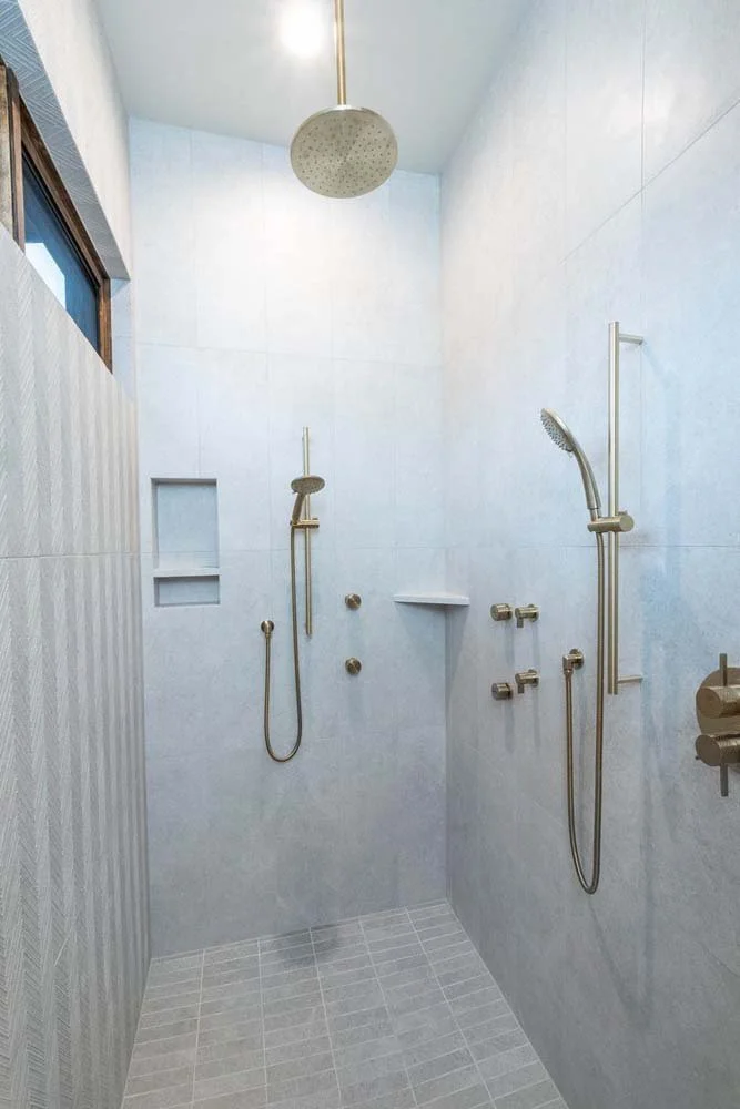 This Pronghorn - Switchback residence, a luxury custom home, showcases its superb interior design with this modern walk-in shower. The space features a sleek design with multiple showerheads, including a rain shower and two handhelds. Built-in niche