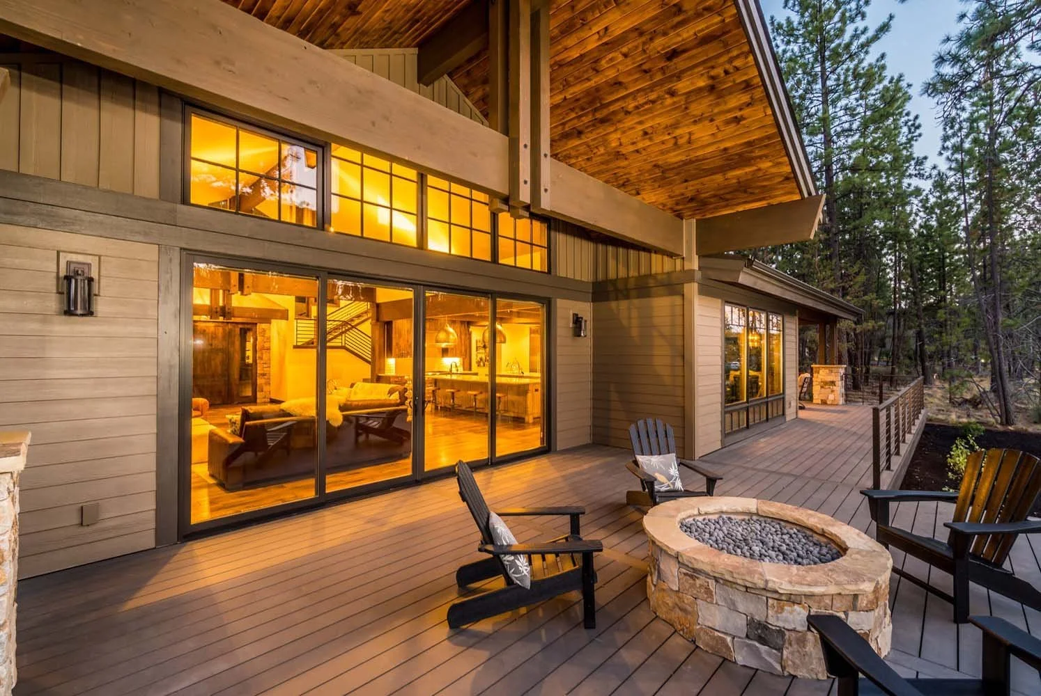 This stunning residence, designed by Spencer Williams, is a masterpiece of architecture. The mountain modern home in Tetherow - Bainbridge Court features large glass sliding doors that lead to a beautiful wooden deck with a fire pit, all set among ta