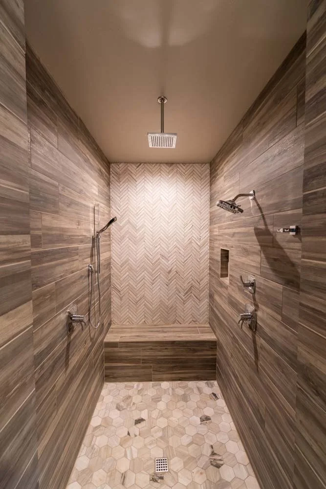 A mountain modern shower stall featuring a bench and dual showerheads. The walls are finished with wood-look tiles and the floor with hexagonal tiles. Part of the award-winning Tetherow - Bainbridge Court project.