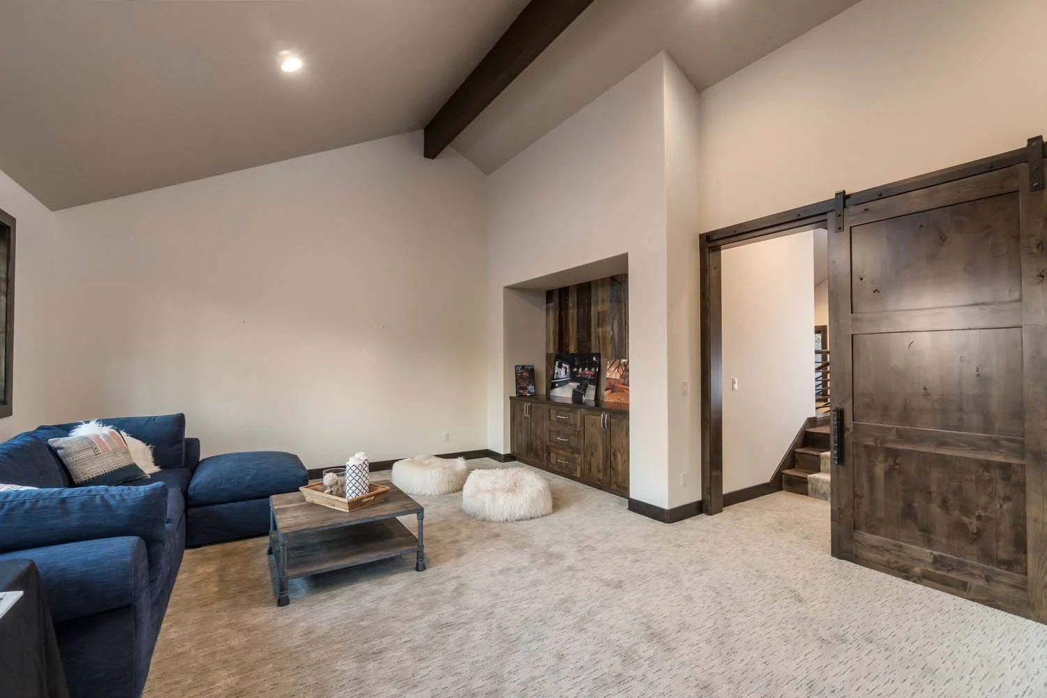Cozy up in this beautiful mountain modern living room from the Tetherow - Bainbridge Court home, designed by Spencer Williams with interiors by Kristy Yozamp. The space features a chic navy sofa, a rustic wooden coffee table, and a sliding barn door