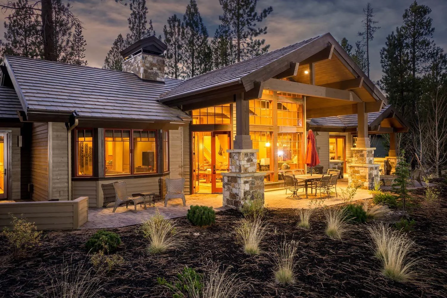 Designed by Spencer Williams, this mountain modern house won "Best of Show" and "Best Architectural Design" for its category. The exterior features a beautiful mix of stone and wood, large windows, and a warm, lit porch with outdoor furniture, set ag