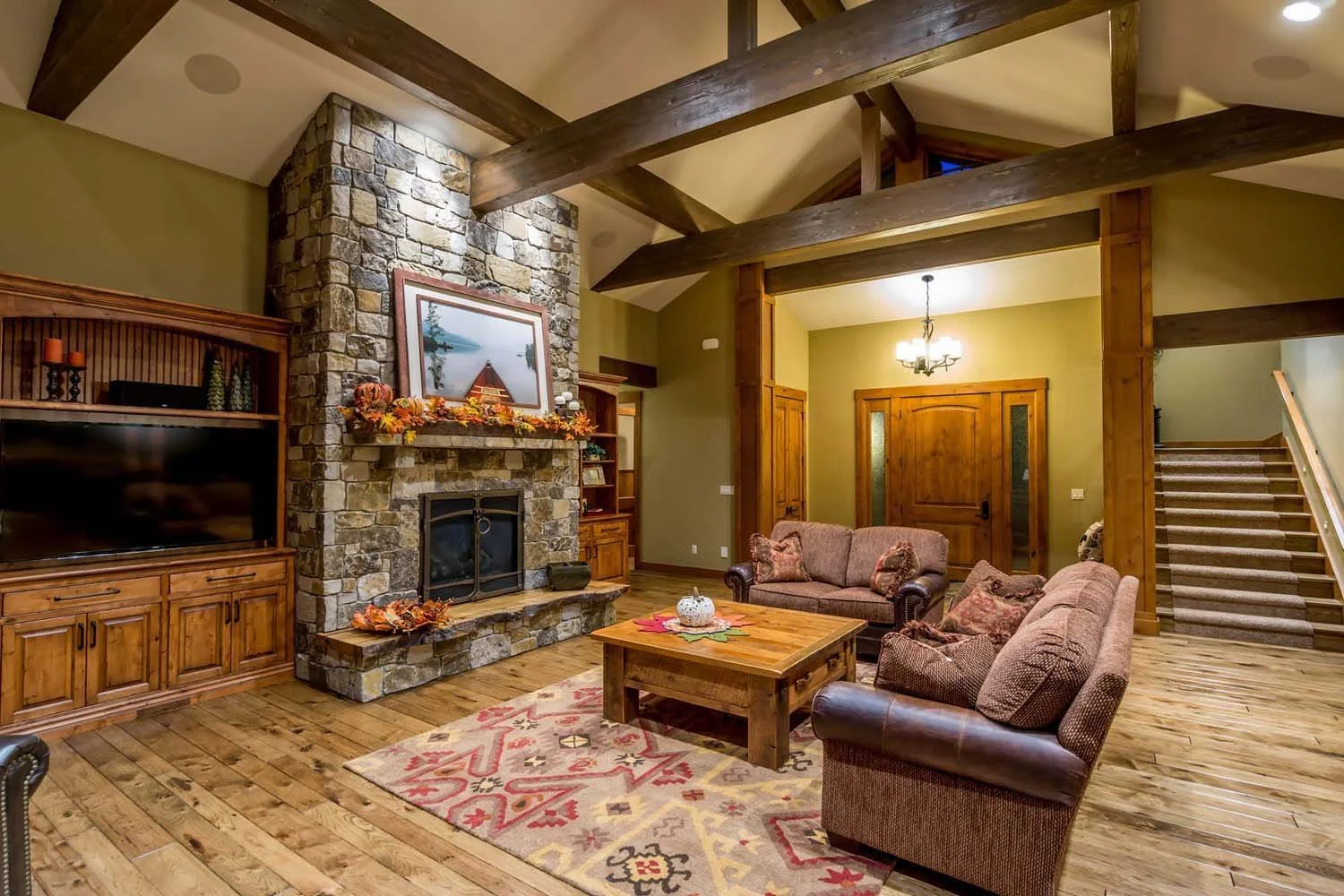 Designed by Spencer Williams, with interiors by Kristy Yozamp, this mountain modern living room won "Best of Show" and "Best Architectural Design." The space features a stunning stone fireplace, a wooden beam ceiling, and a chandelier, with warm fall