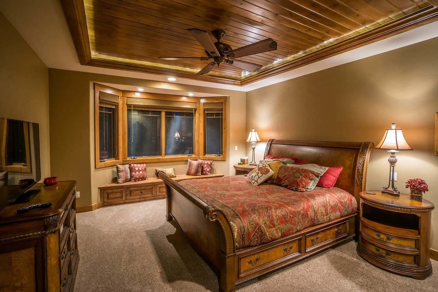Designed by Spencer Williams with interiors by Kristy Yozamp, this cozy bedroom won "Best of Show" and "Best Interior Finish." The space features a beautiful wooden bed, a built-in window seat, and warm wood paneling on the ceiling, creating a perfec