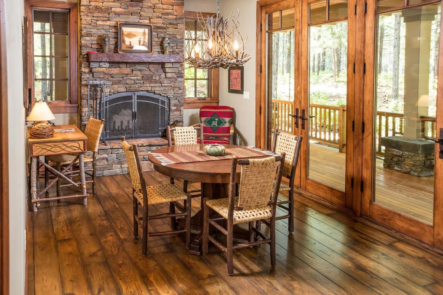 This rustic dining room in Black Butte Ranch - Foin Follette is a true Central Oregon retreat. The space, with its wooden floors, stone fireplace, and a round wooden table, offers a cozy and inviting atmosphere. A unique chandelier made of tree branc