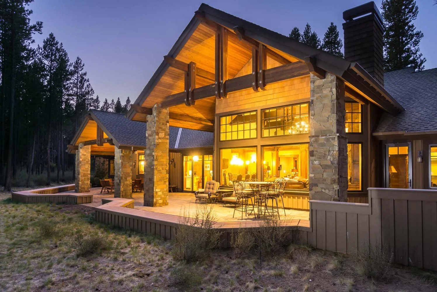 This luxury custom home in Caldera Springs - Trailmere Circle is a masterpiece of architecture design by Spencer Williams. The modern house features a large, illuminated outdoor patio area with stone pillars, blending seamlessly with the surrounding
